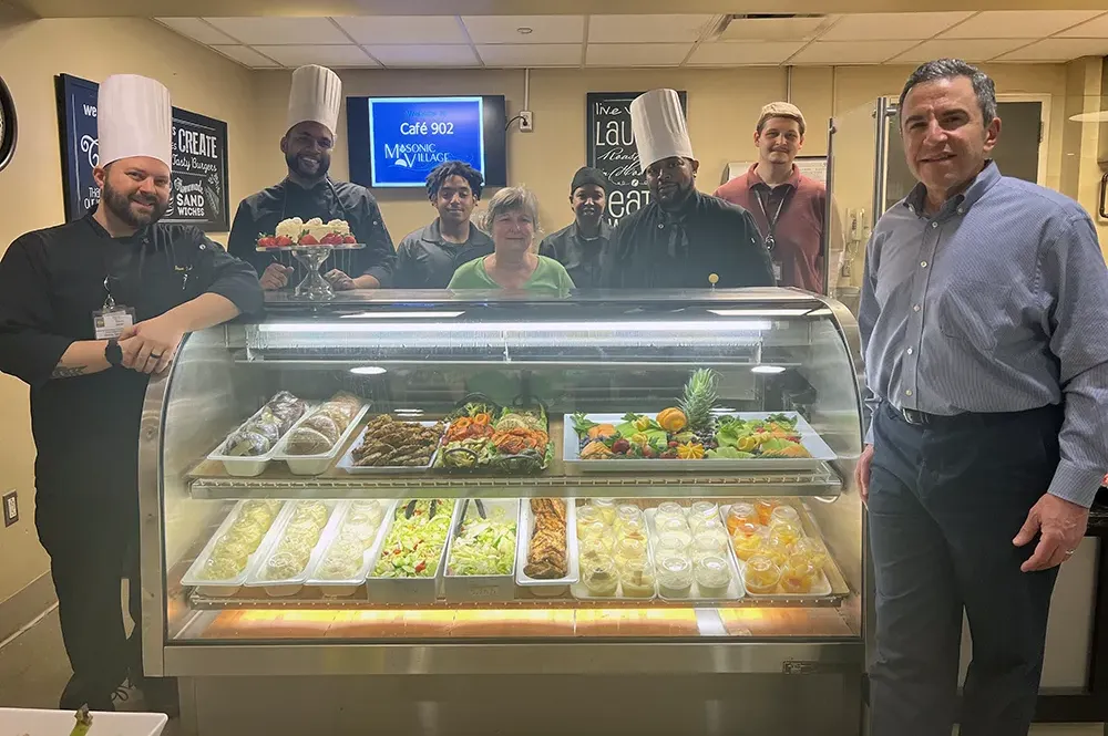 staff and residents standing around the food case at cafe 902